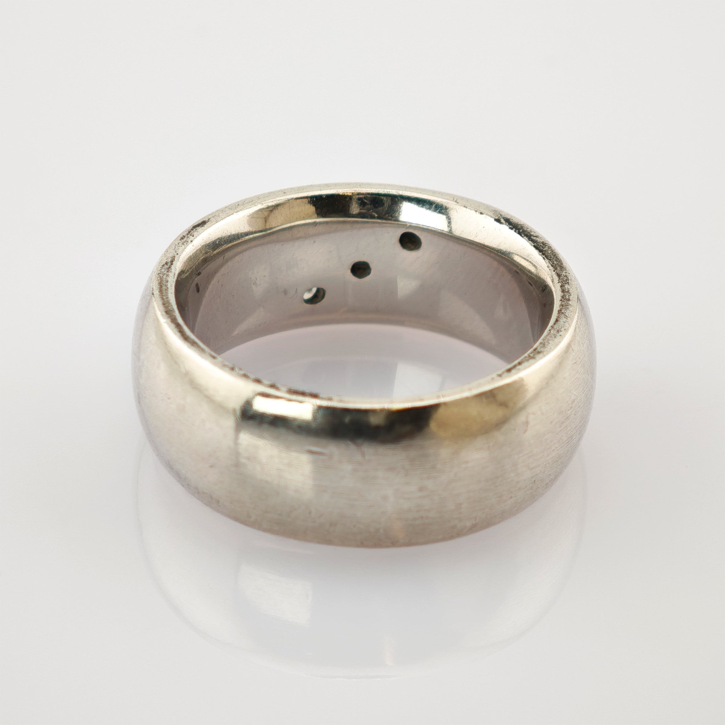 Silberner Ring mit glatter Außenseite und Löchern im inneren Band auf weißem Hintergrund