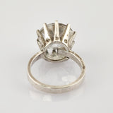 Silberner Ring mit großem klarem Edelstein in Kronenfassung auf weißem spiegelndem Hintergrund.