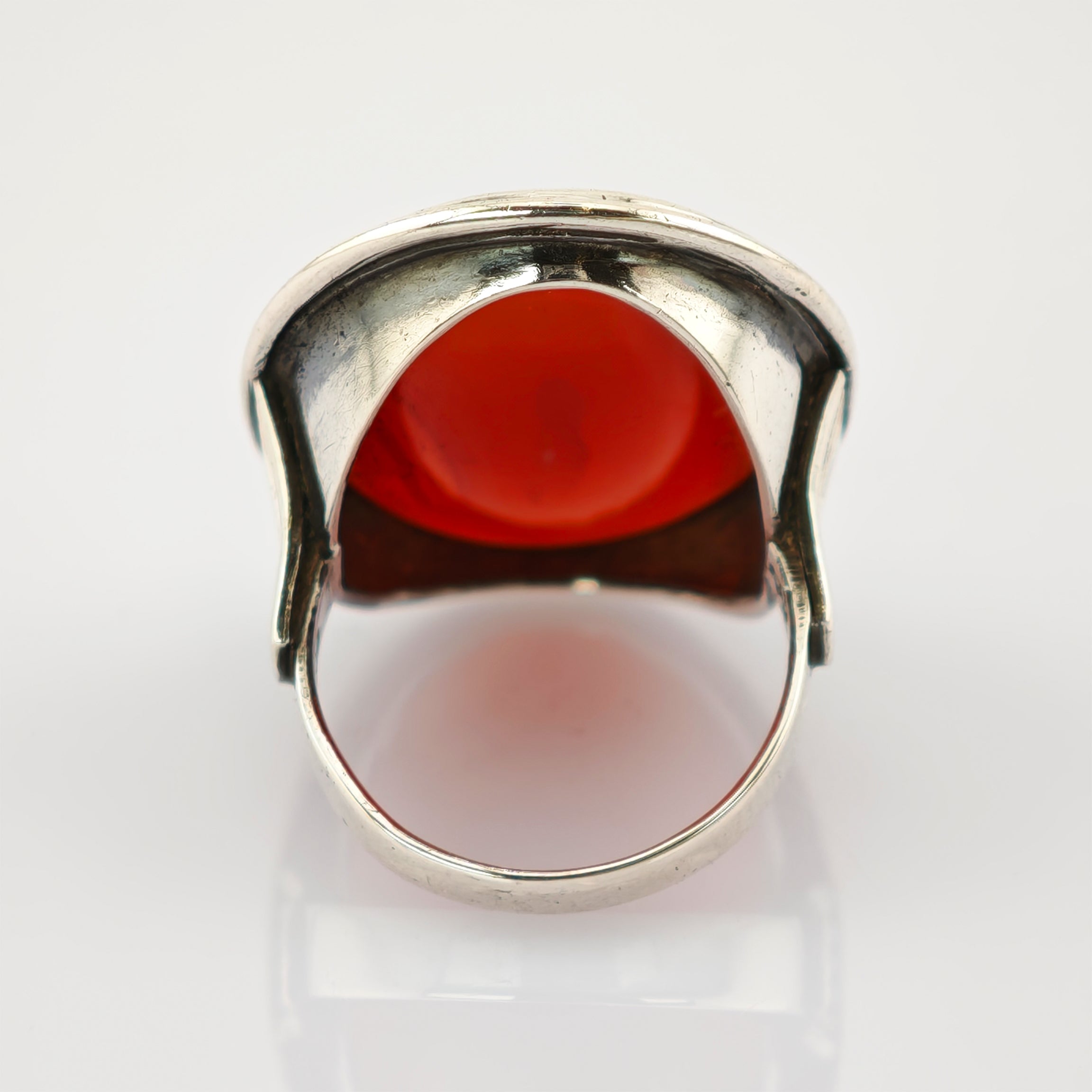 Silberner Ring mit großem, glattem roten ovalen Stein auf reflektierendem weißen Hintergrund.