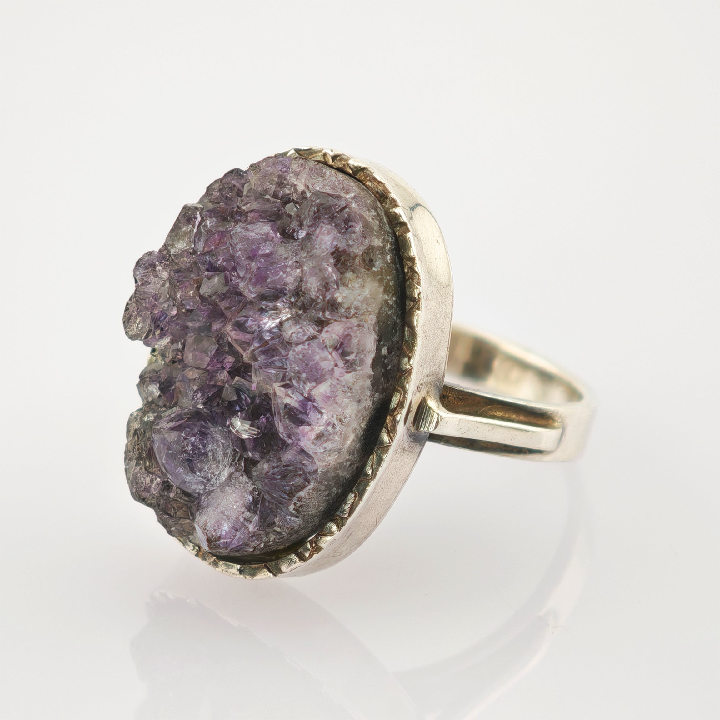 Silberner Ring mit grobem lila Kristall und glatter Bandstruktur auf weißem Hintergrund.