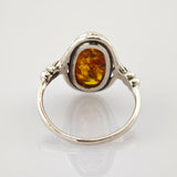 Silberner Ring mit ovalem Bernstein und filigraner Metallverzierung auf weißem Hintergrund