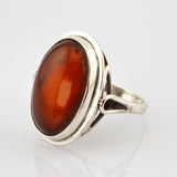 Silberner Ring mit großem ovalem Bernstein in Orange-Braun auf weißem Hintergrund