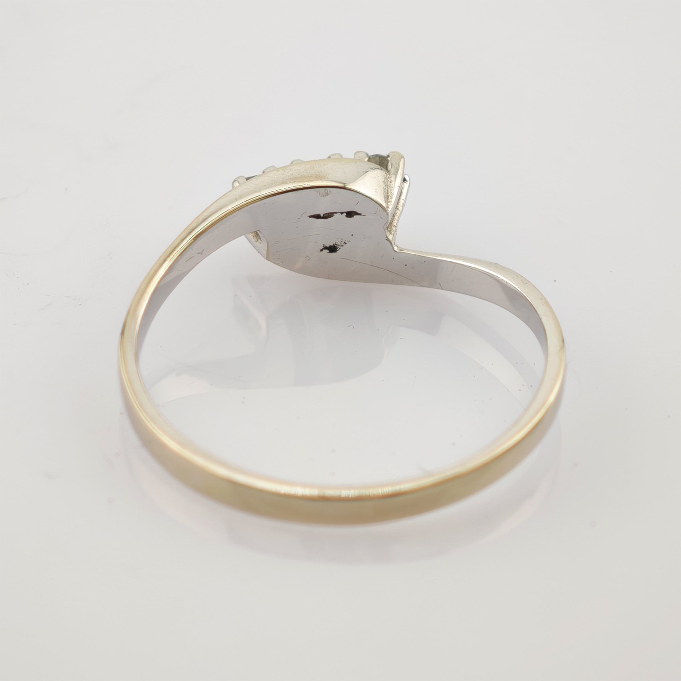 Silberner Ring mit ovalem Besatz und kleinen Perlen auf weißer reflektierender Fläche.