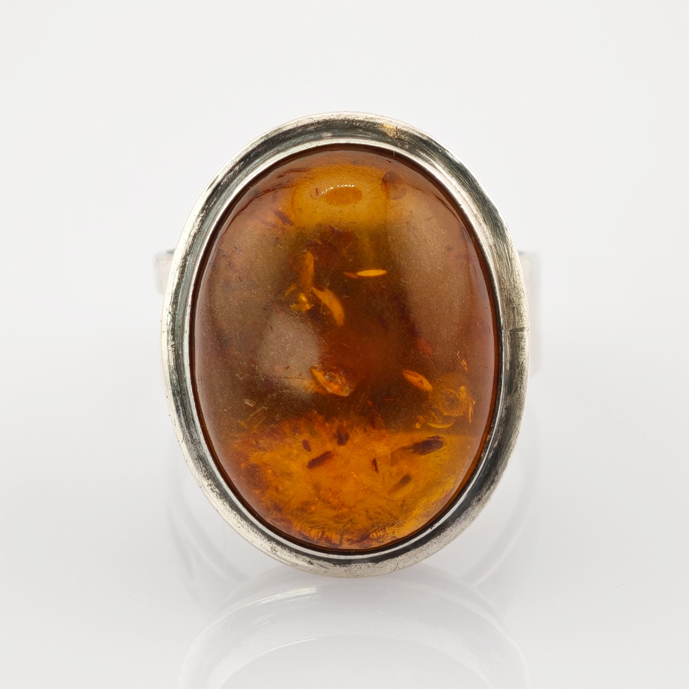 Silberner Ring mit großem ovalem Bernstein und natürlichen Einschlüssen auf weißem spiegelndem Untergrund