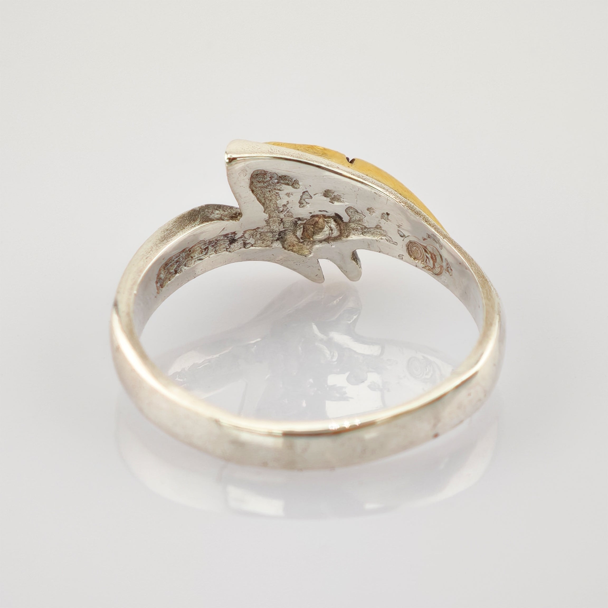 Nahaufnahme eines silbernen Rings mit oxidierter Innenseite und gelblicher, eingekerbter Oberseite auf weißem Hintergrund.