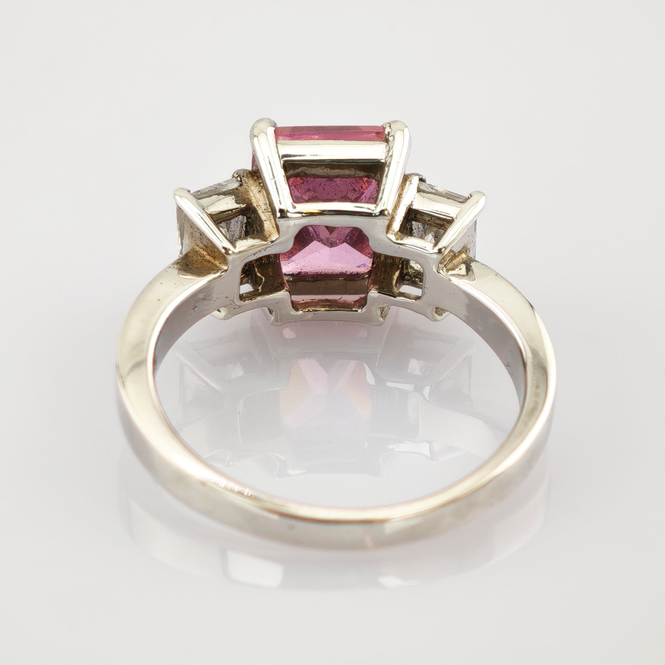 Silberner Ring mit pinkem Edelstein und kleinen klaren Steinen auf reflektierendem Hintergrund