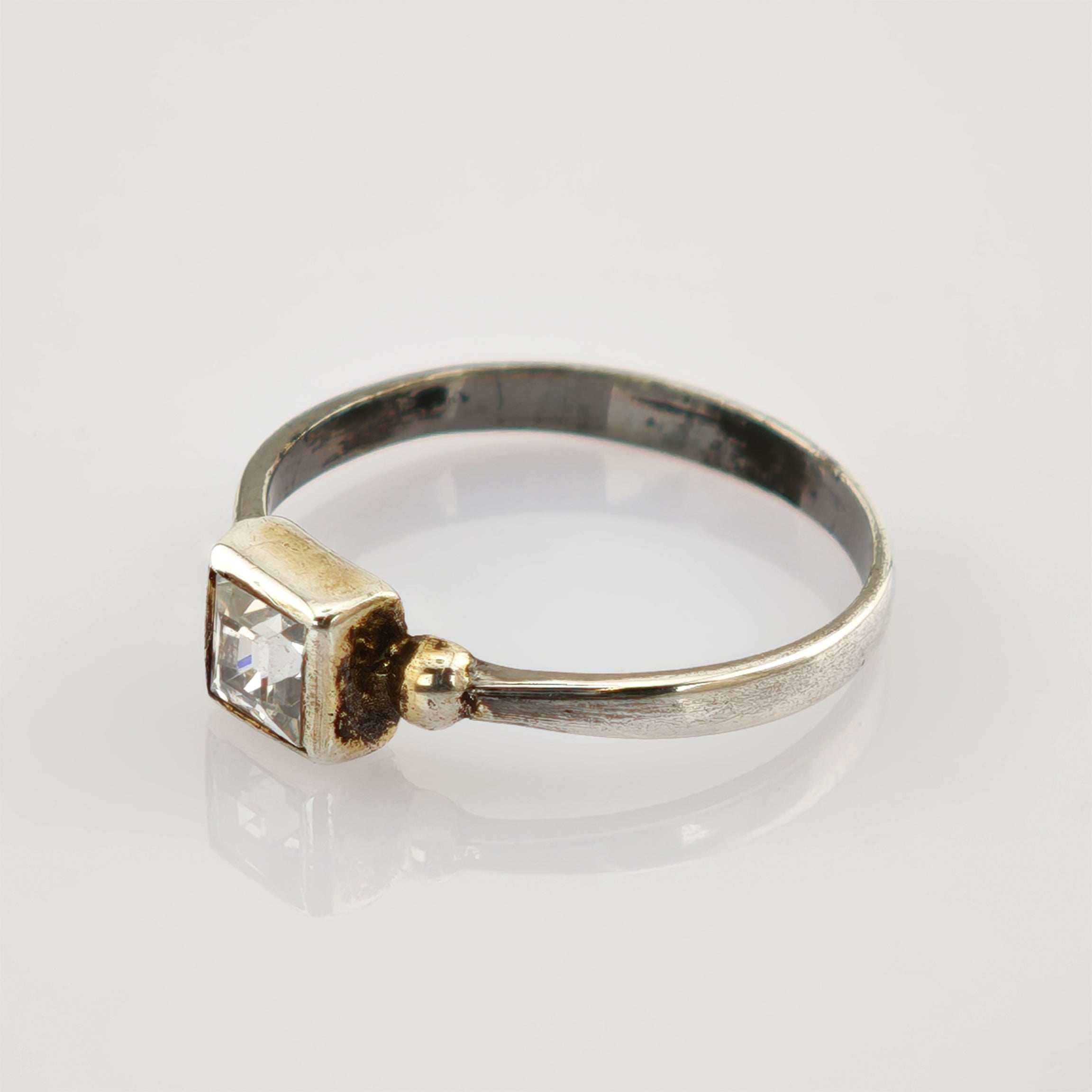Silberner Ring mit quadratischem, klarem Kristallstein auf reflektierender Oberfläche