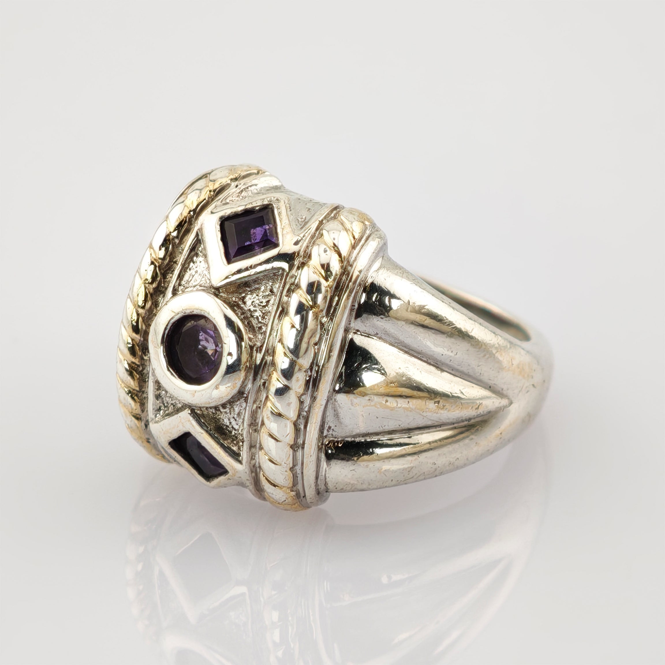 Silberner Ring mit kunstvollem Reliefmuster und drei kleinen lila Edelsteinen.