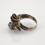 Silberner Ring mit Scheibenkopfmotiv und Hörnern auf hellem, grauem Hintergrund.