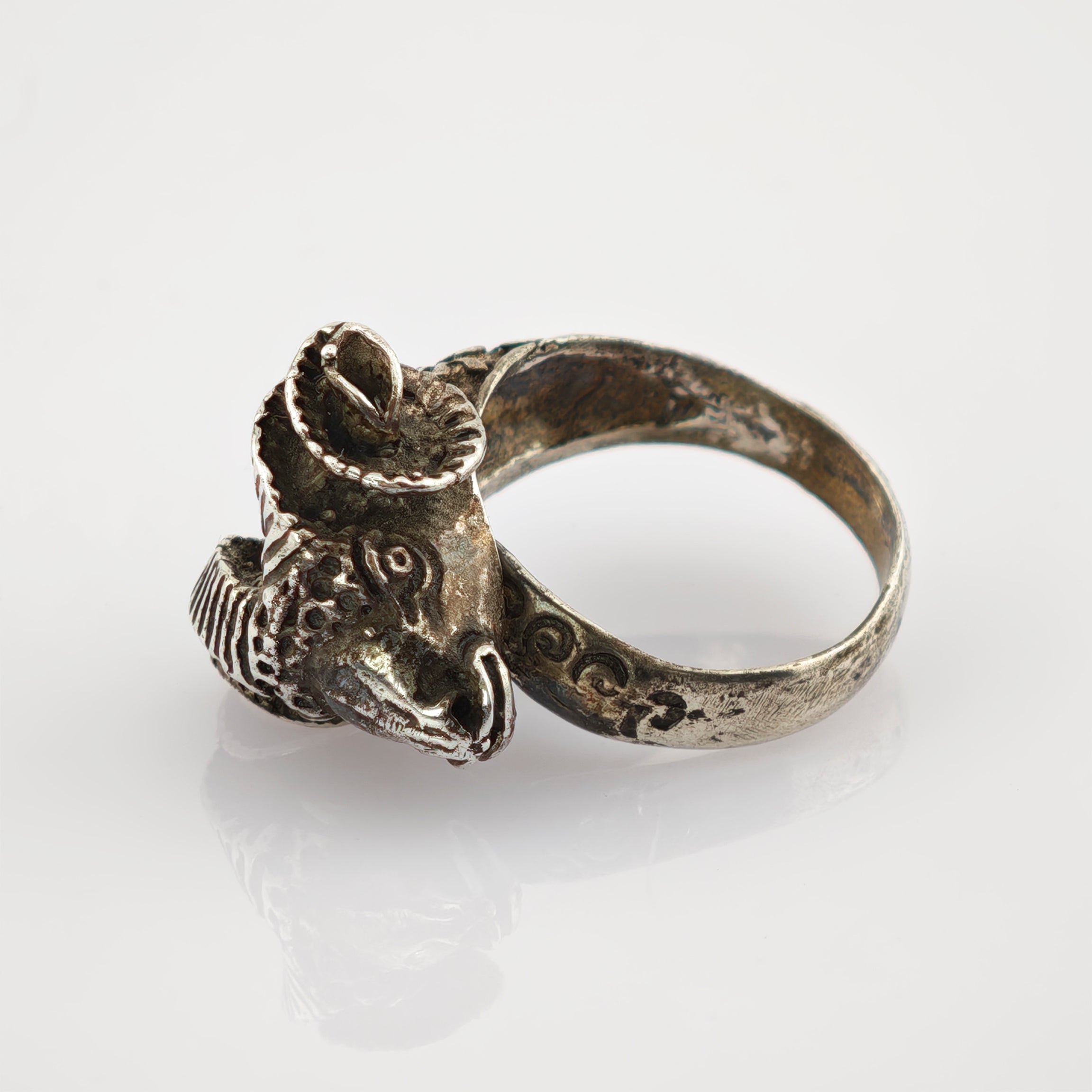 Silberner Ring mit Scheibenkopfmotiv und Hörnern auf hellem, grauem Hintergrund.