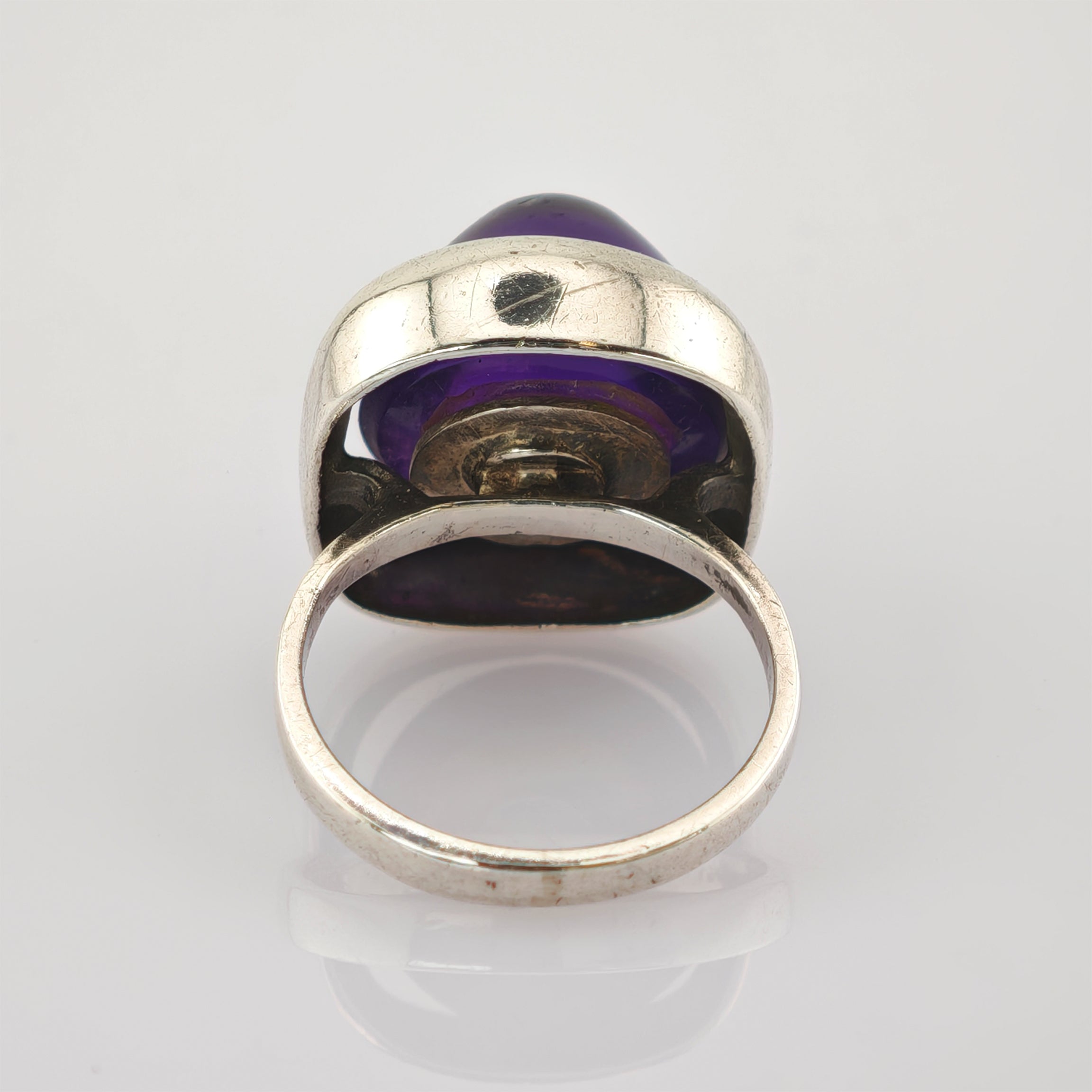 Silberner Ring mit großem rundem violettem Edelstein und sichtbaren Gebrauchsspuren auf dem Band.