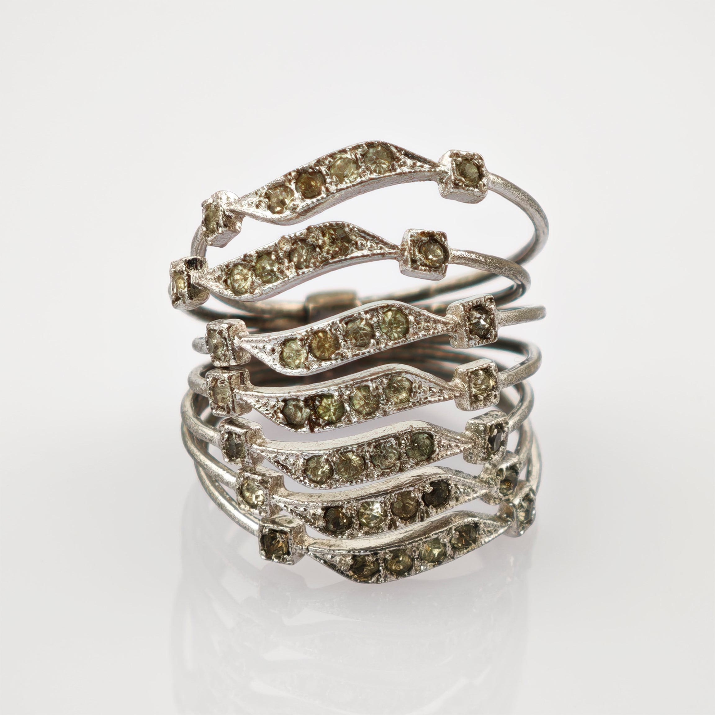 Silberner Ring mit sechs wellenförmigen Bändern und hellgrünen Steinen an einem Finger.