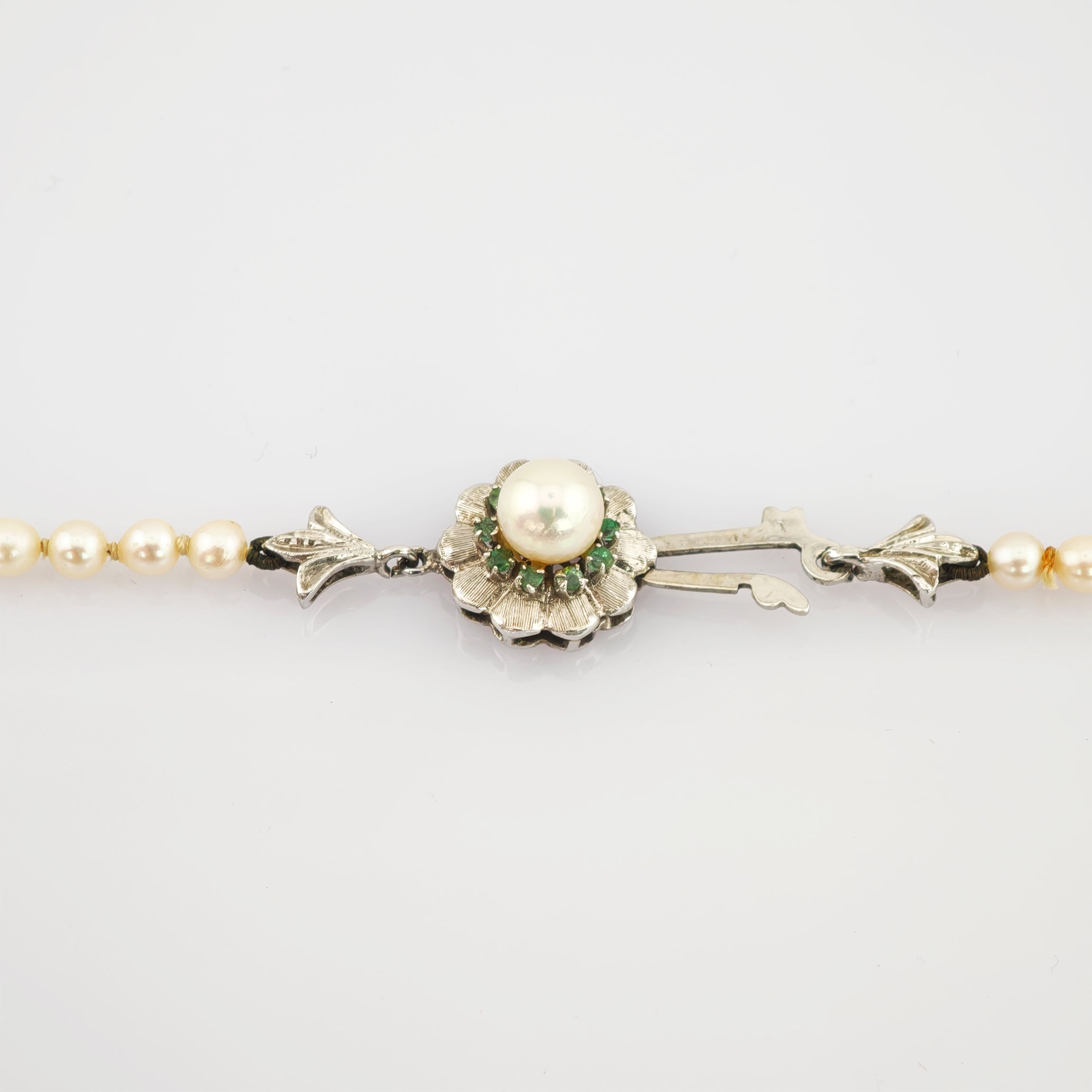 Nahaufnahme eines silbernen Schmuckverschlusses mit zentraler Perle und grünen Edelsteinen im Blumenmotiv.