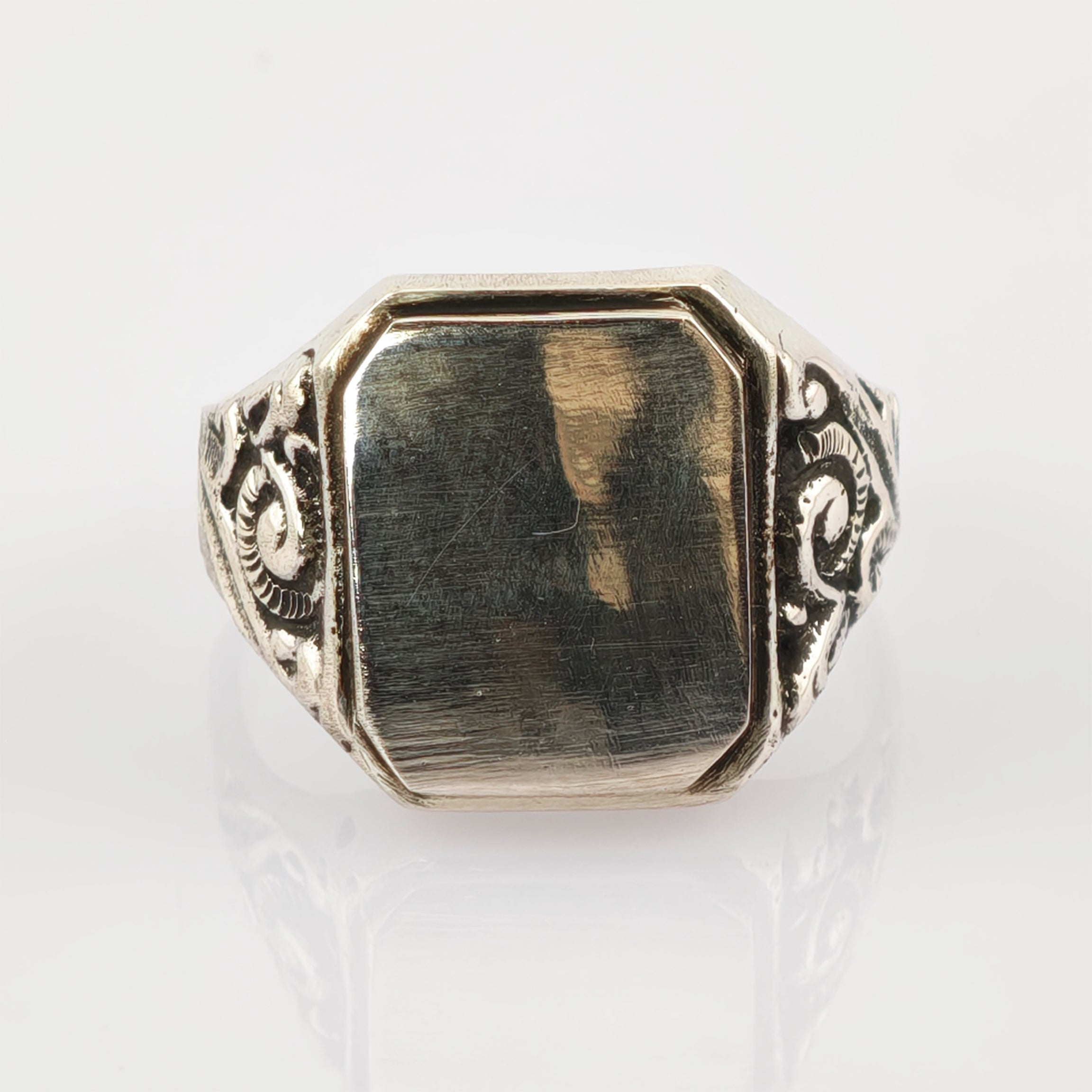 Silberfarbener Signet-Ring mit rechteckigem, facettiertem Gesicht und floralen Verzierungen auf weißem Hintergrund.