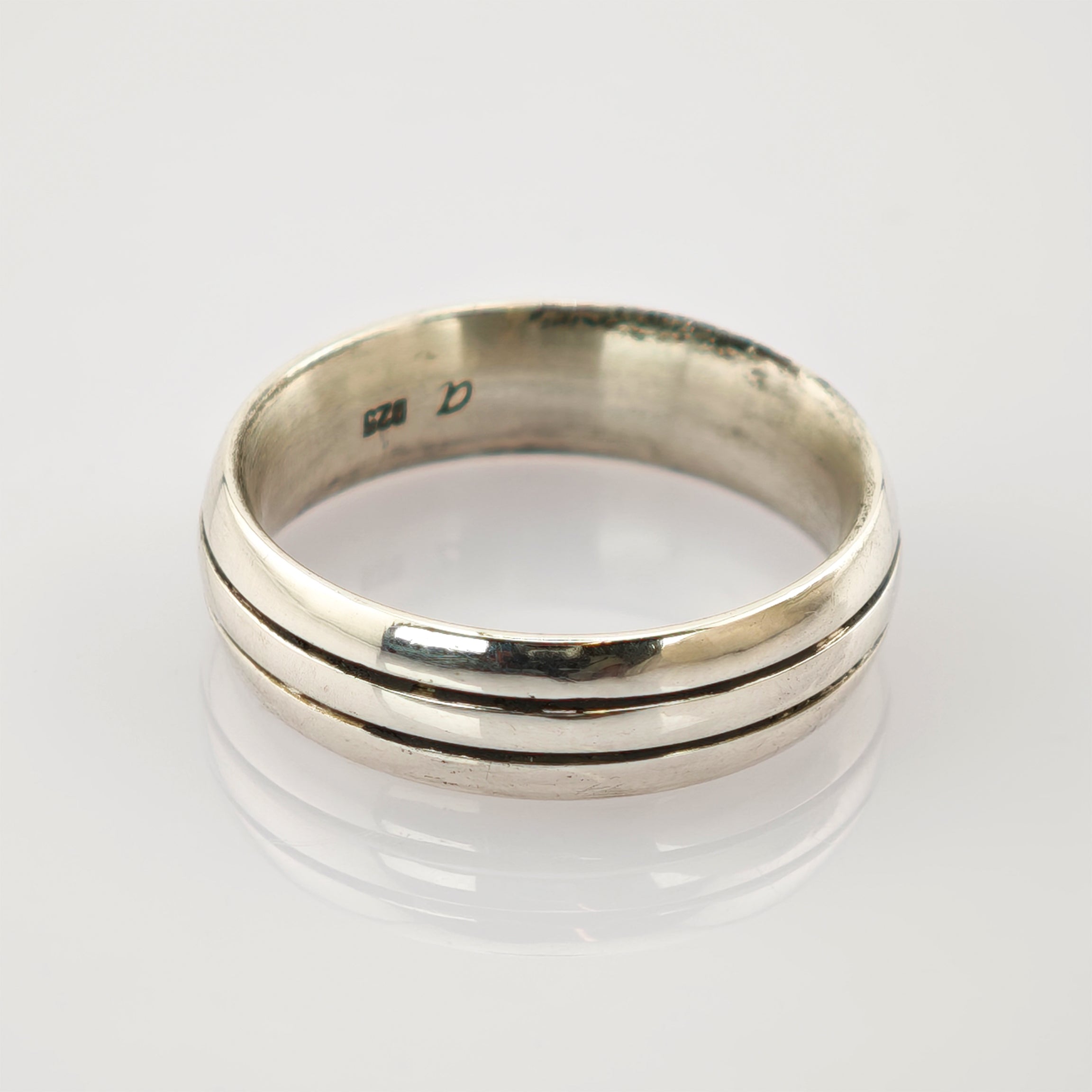 Silberner Vintage-Ring mit zwei parallel verlaufenden Rillen und leichter Patina auf weißem reflektierendem Untergrund.