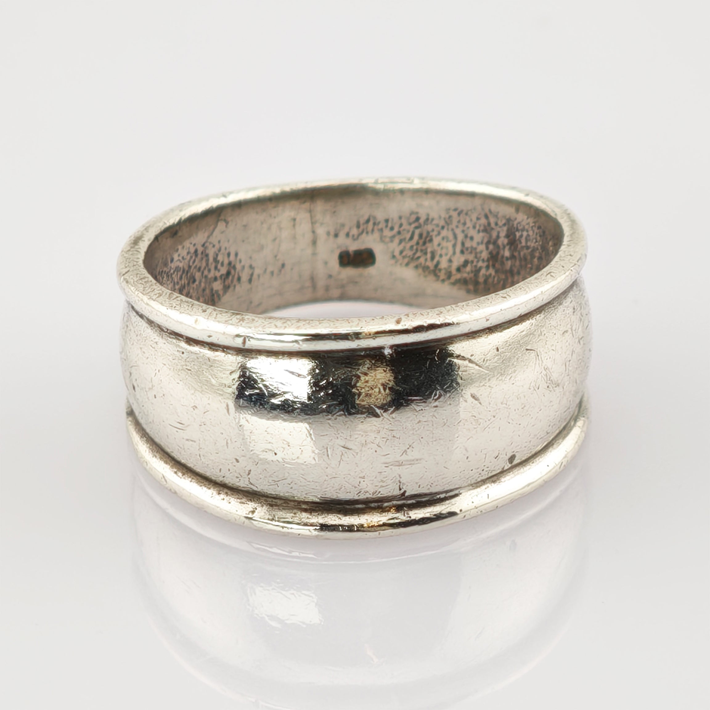 Silberner Vintage-Ring mit rundem Band und Gebrauchsspuren auf reflektierender Oberfläche.