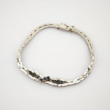 Silbernes Armband mit Diamantmuster und kleinen dunklen Edelsteinen in zwei mittleren Abschnitten.