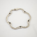 Silbernes Armband mit doppelter Kettenoptik und kleinen schwarzen runden Edelsteinen auf weißem Hintergrund.