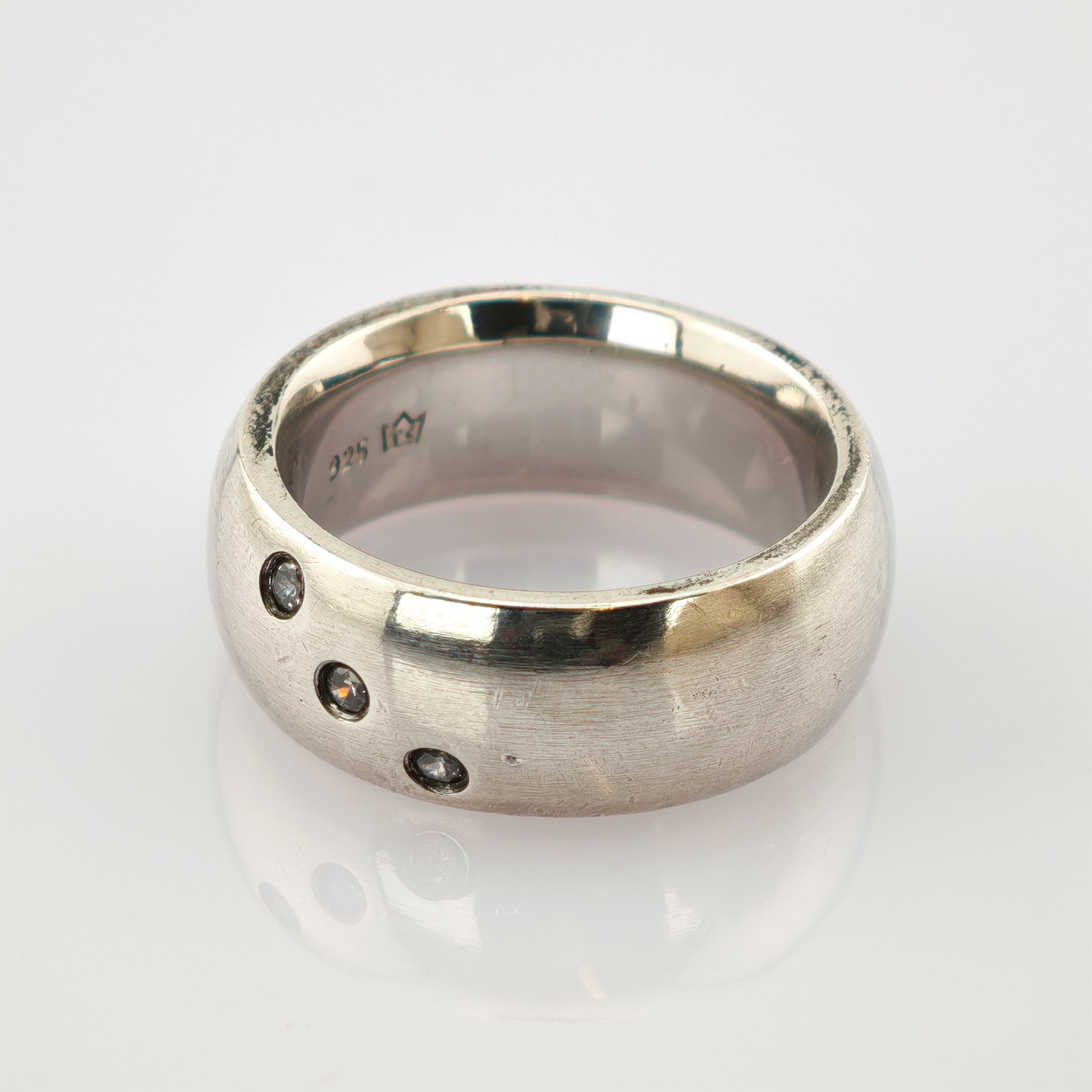 Silberring aus 925er Sterlingsilber mit drei kleinen eingelassenen Steinen auf weißer Oberfläche