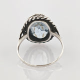 Silberring mit facettiertem blauem Edelstein und Seilrand auf weißer Oberfläche