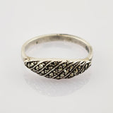 Silberring mit diagonalen Rillen und kleinen funkelnden Steinen auf hellem, spiegelndem Hintergrund