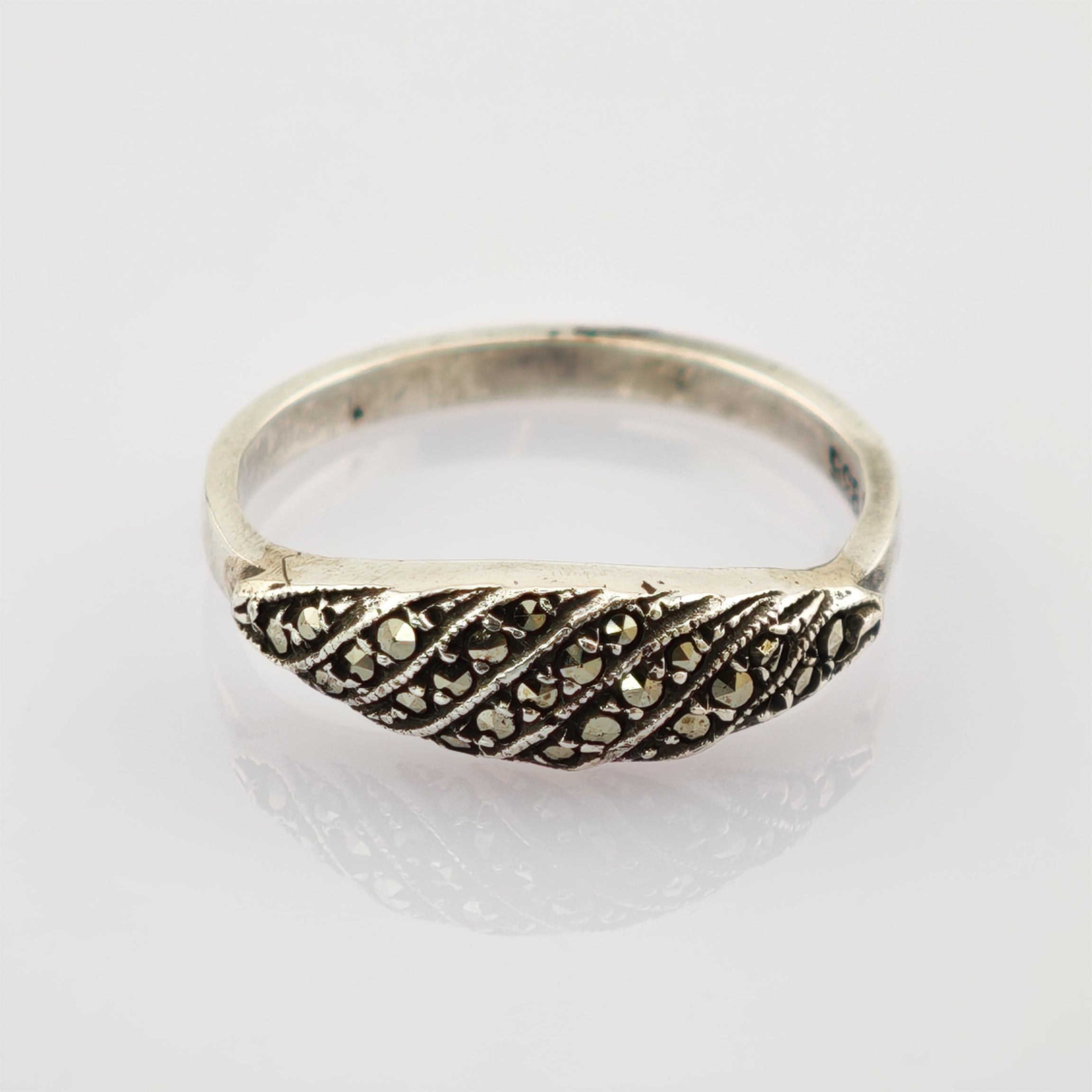 Silberring mit diagonalen Rillen und kleinen funkelnden Steinen auf hellem, spiegelndem Hintergrund
