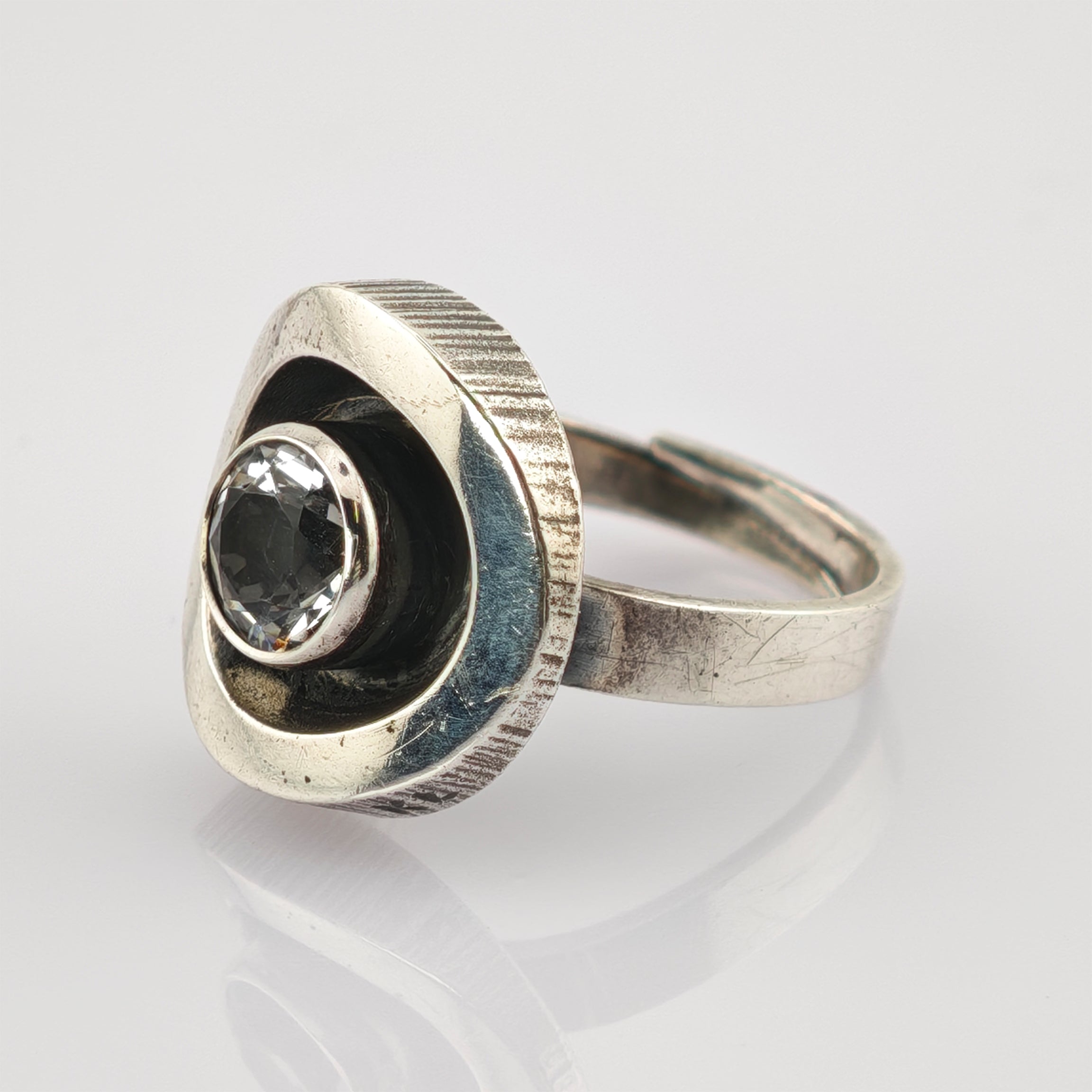 Silberring mit dreieckigem Oberteil und facettiertem, klarem Edelstein, trägt Kratzer und Patina.
