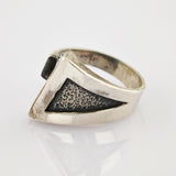 Silberring mit dreieckiger schwarzer Textureinlage auf reflektierender Oberfläche vor weißem Hintergrund.