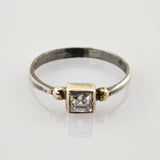 Silberring mit dünnem Band und quadratischen klaren Edelstein, verziert mit goldenen Perlen.