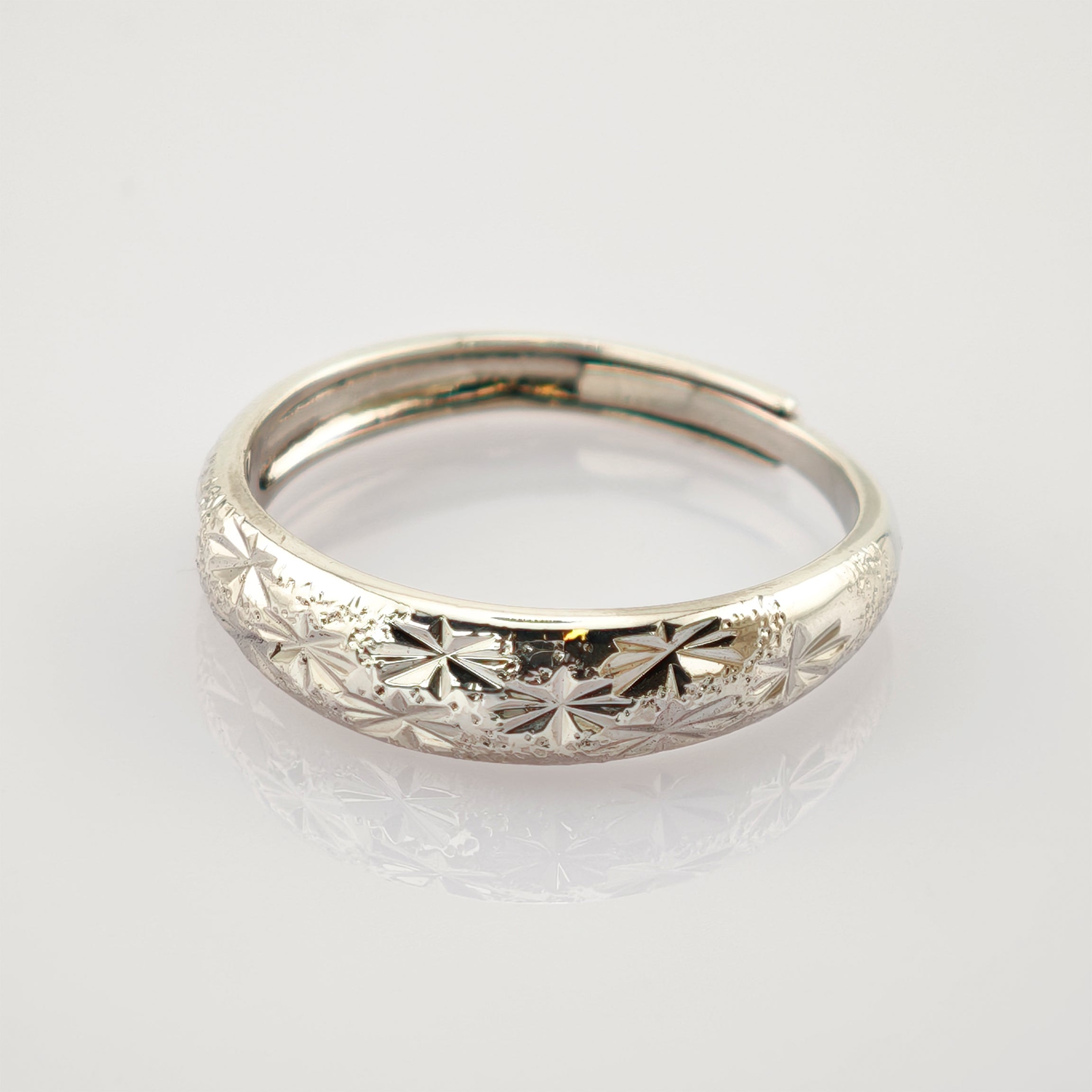 Silberfarbener Edelstahlring mit eingravierten Stern- und Blumenmustern auf der abgerundeten Oberfläche.