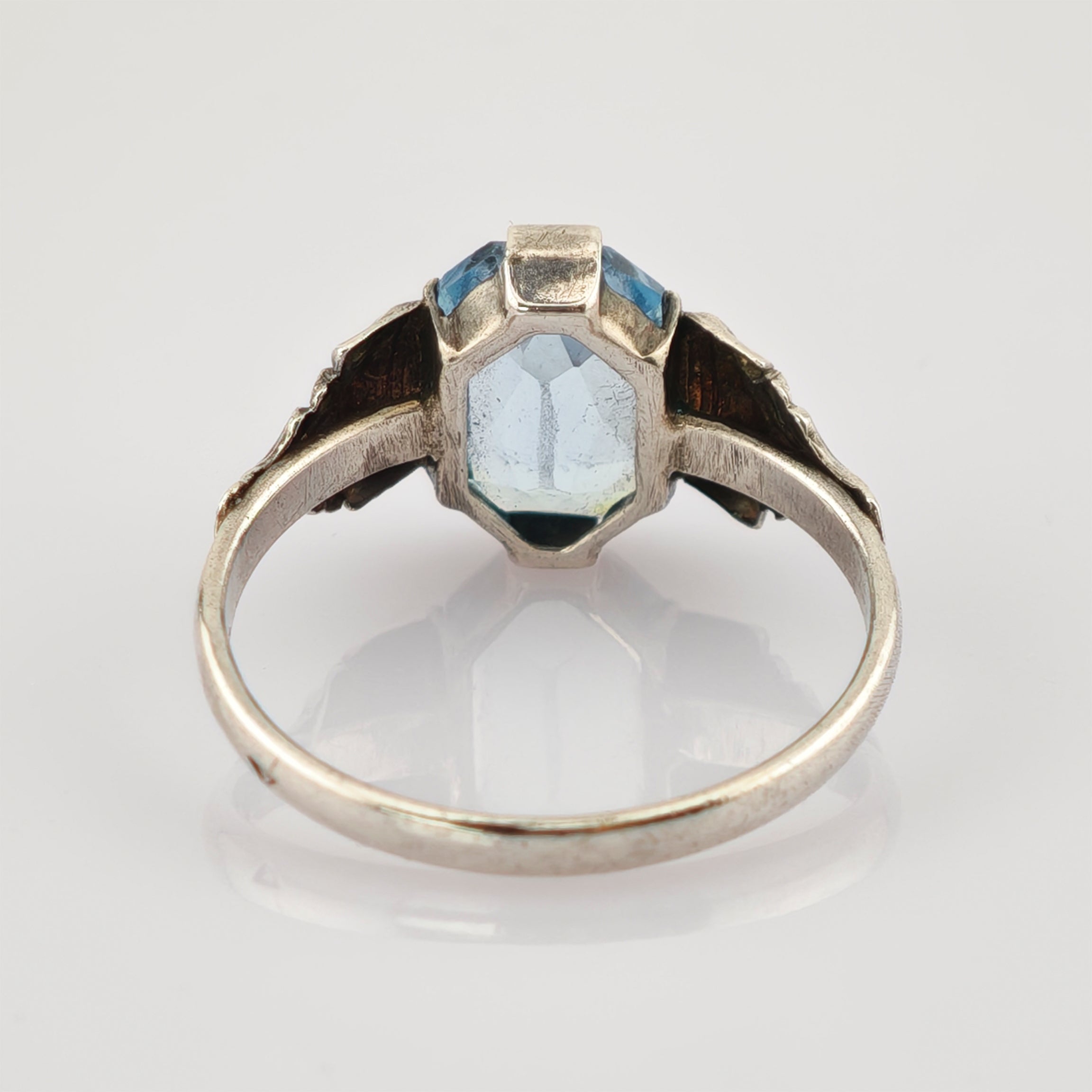 Rückseite von elegantem silbernernen Ring mit blauem trapezförmigem Edelstein und floralen Verzierungen.