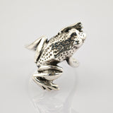 Silberring in Froschform mit texturiertem Rücken und glatten Beinen auf weißem Untergrund.