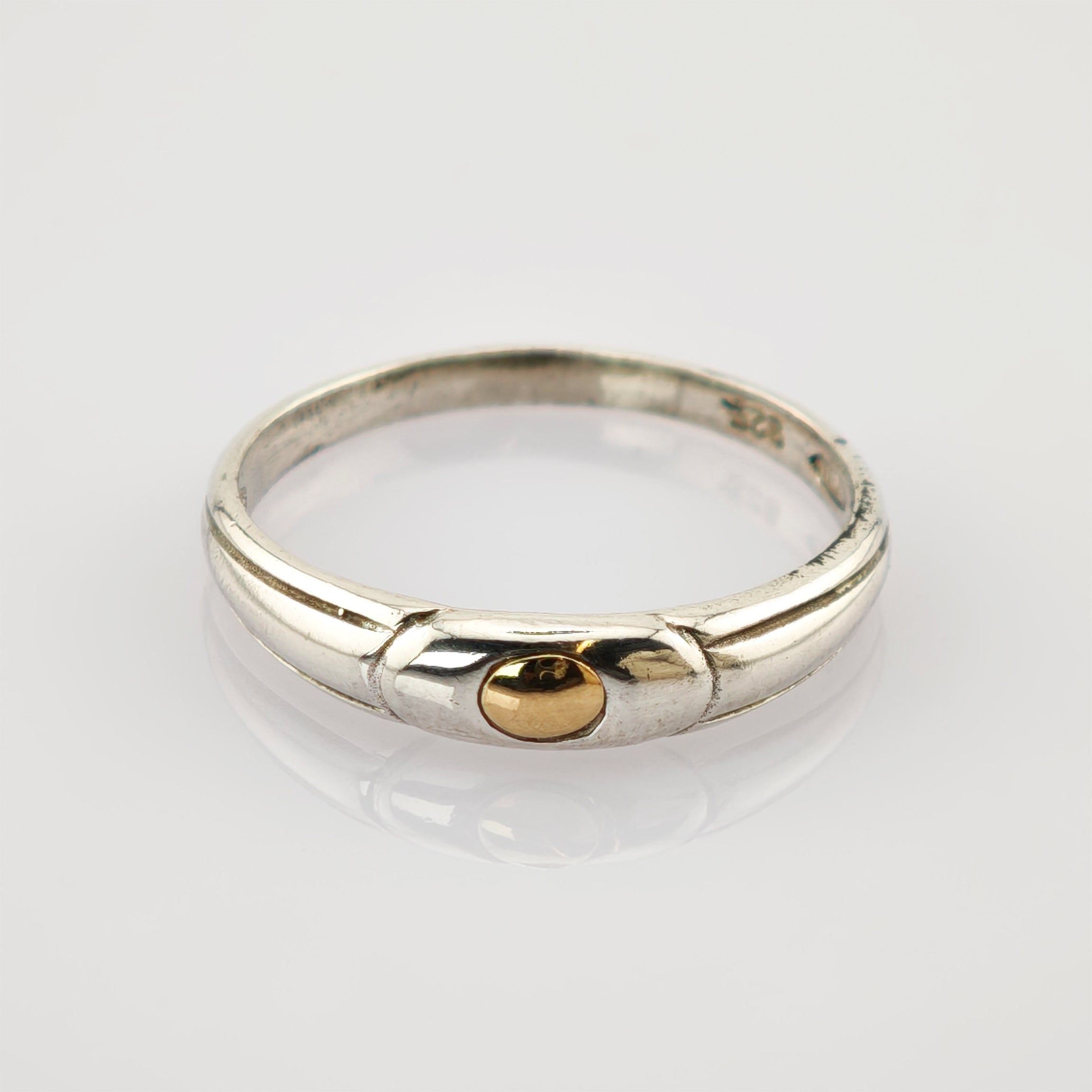 Silberring mit goldenem rundem Element in der Mitte auf reflektierender weißer Oberfläche