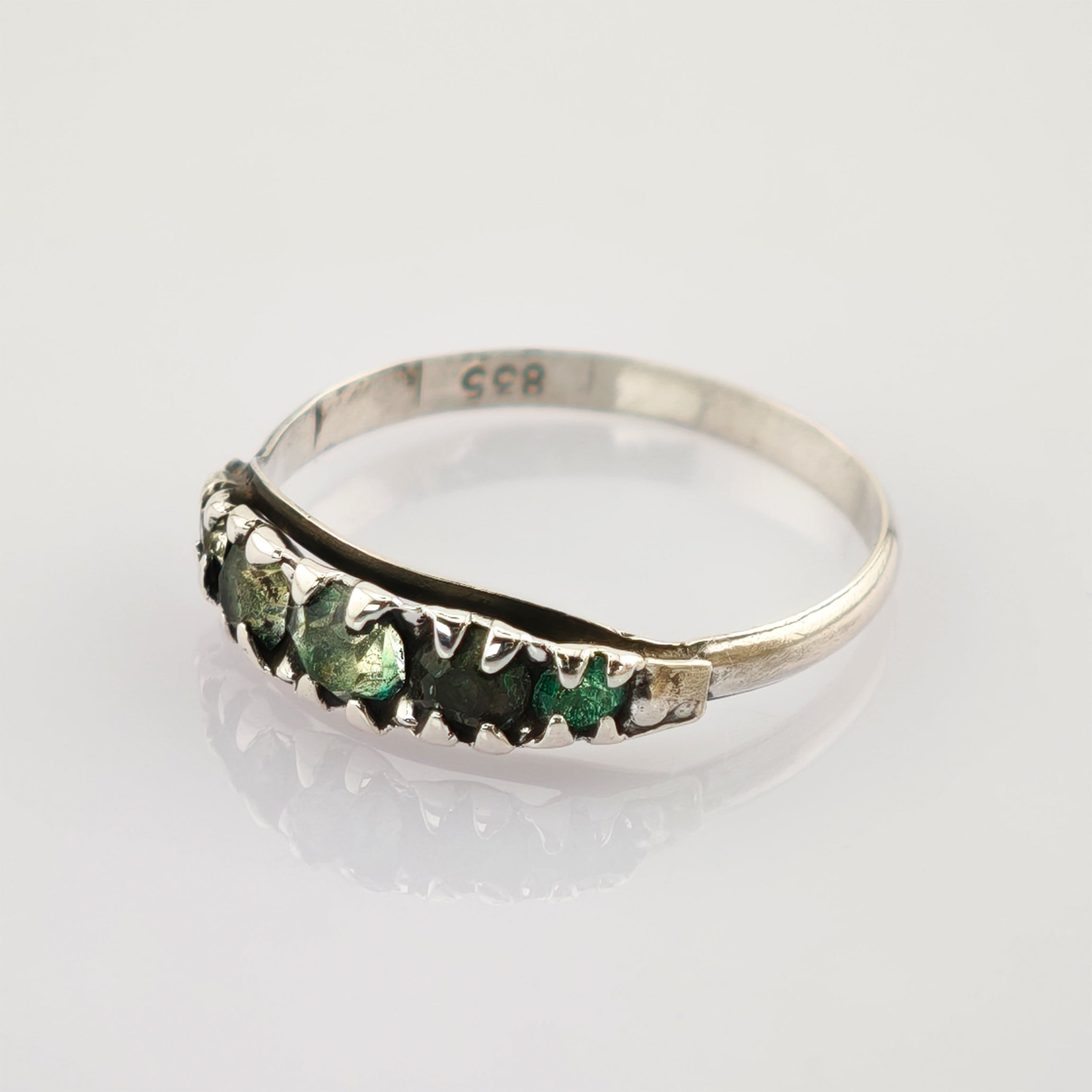 Silberring mit unregelmäßigen grünen Steinen und 835er Punze, auf weißem Untergrund.