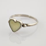 Silberring mit herzförmigem cremefarbenem Zentrum auf glänzender Oberfläche vor hellgrauem Hintergrund