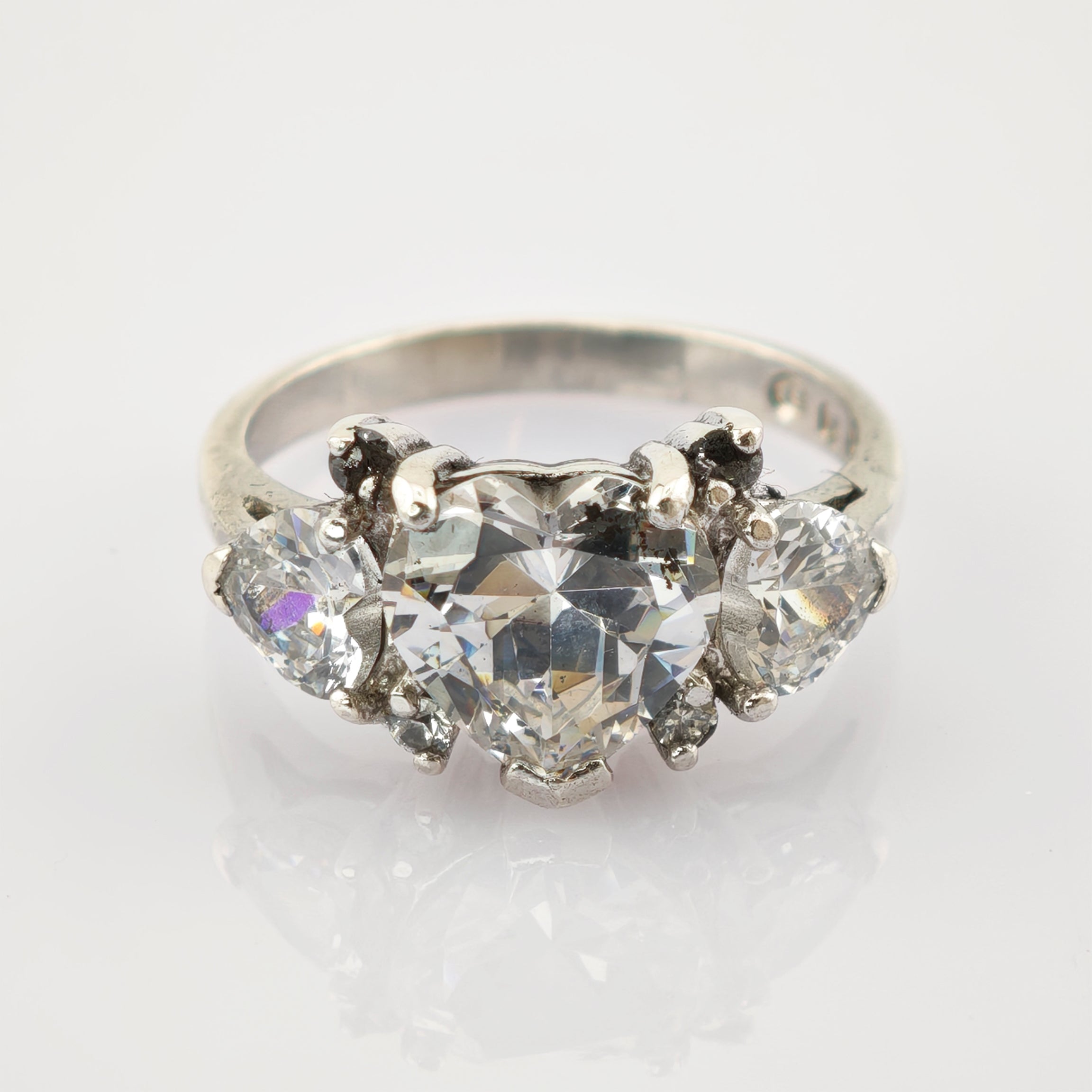 Silberring mit herzförmigem zentralem Diamanten und zwei birnenförmigen Diamanten auf reflektierendem Hintergrund