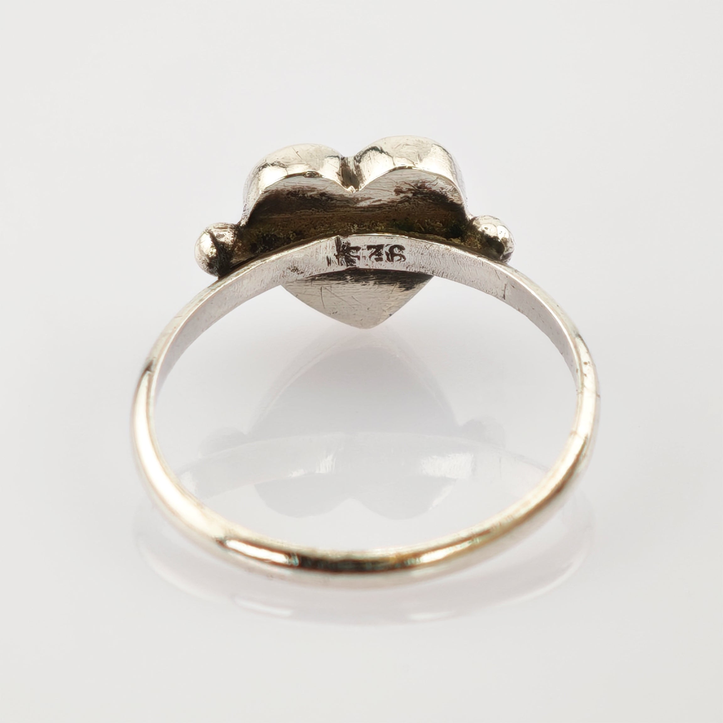Silberring mit Herzform und 925-Punze, sichtbare Kratzer und Anlaufspuren, auf weißem Hintergrund.