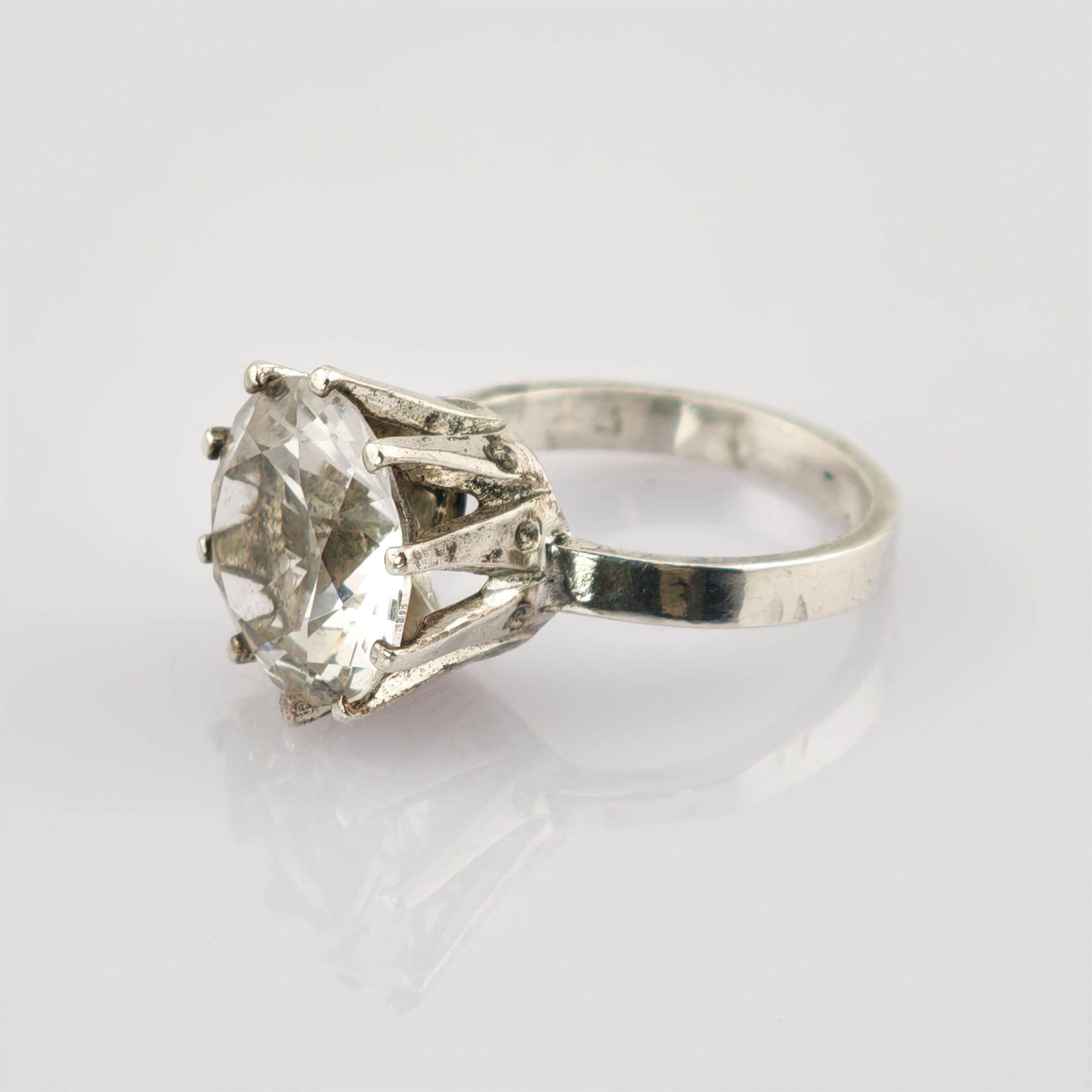 Silberring mit großem klarem facettiertem Schmuckstein in Krappenfassung auf reflektierendem Untergrund