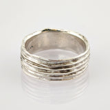 Silberring mit fünf horizontalen Erhebungen auf reflektierender weißer Oberfläche