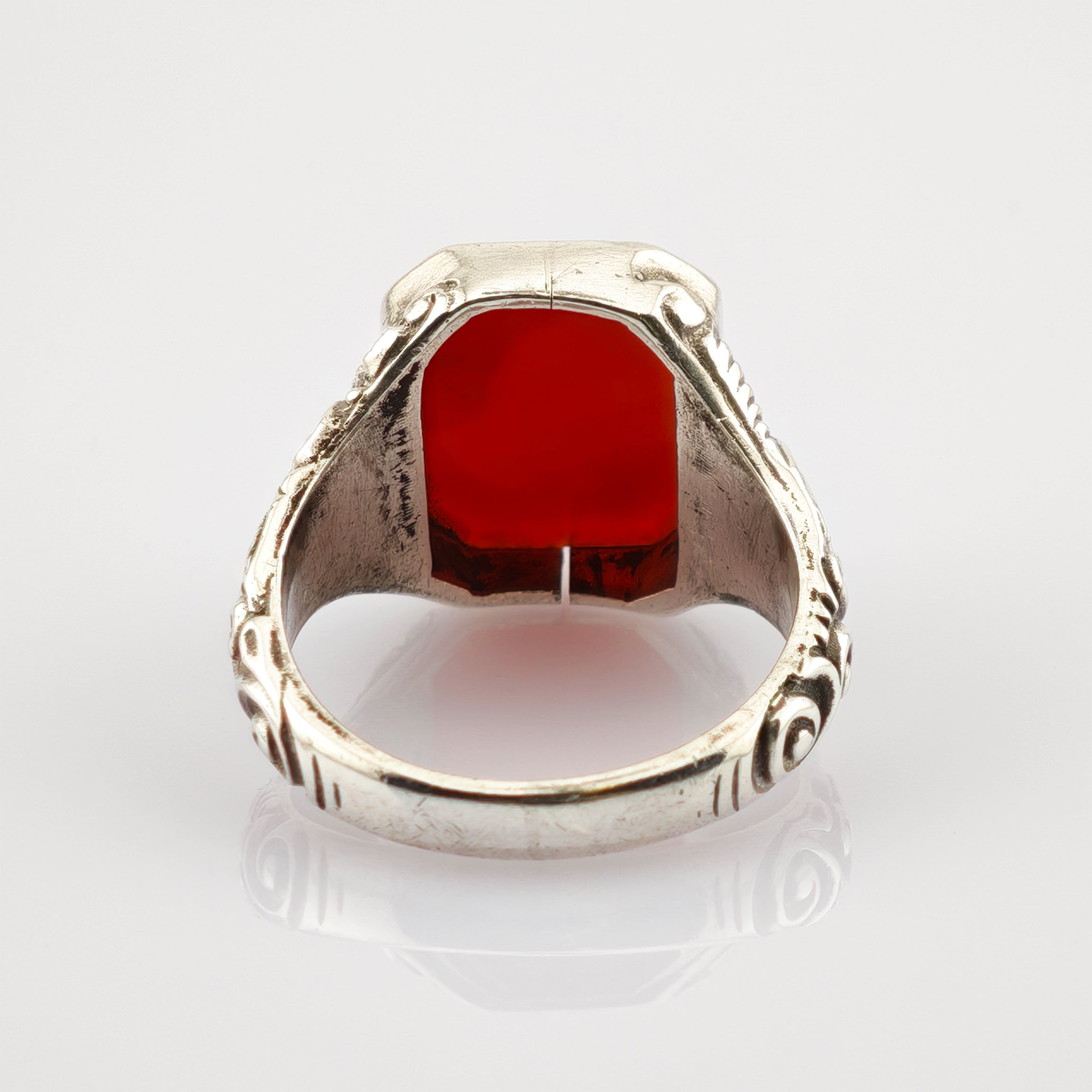 Silberring mit kunstvollen Gravuren und großem facettiertem rotem Edelstein auf weißem Hintergrund