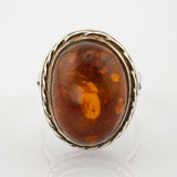 Silberring mit großem ovalem Bernstein in gedrehter Fassung vor weißem Hintergrund.