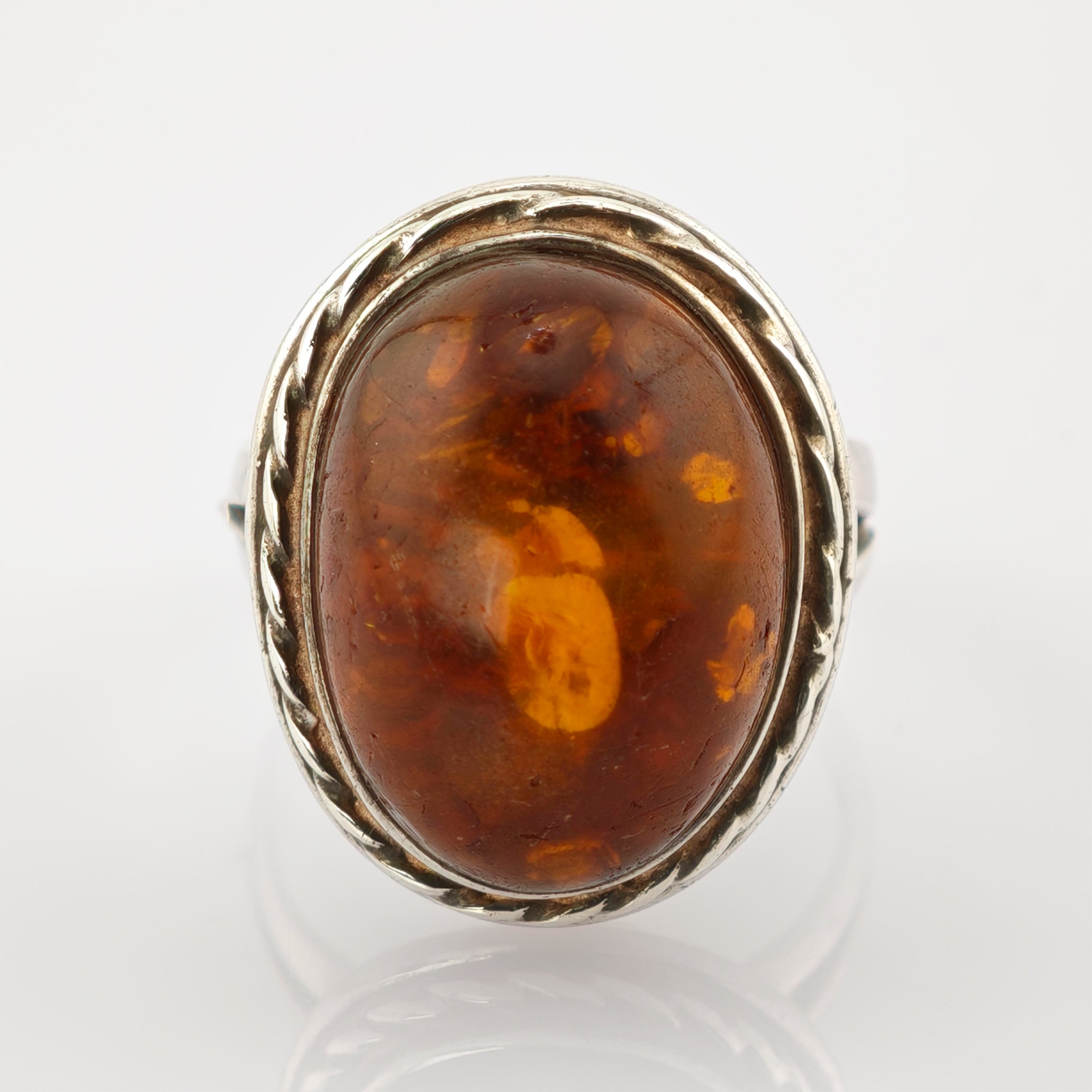 Silberring mit großem ovalem Bernstein in gedrehter Fassung vor weißem Hintergrund.