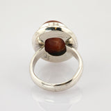 Silberfarbener Vintage-Ring mit großem ovalem rotbraunem Stein in Zargenfassung auf weißem Hintergrund.