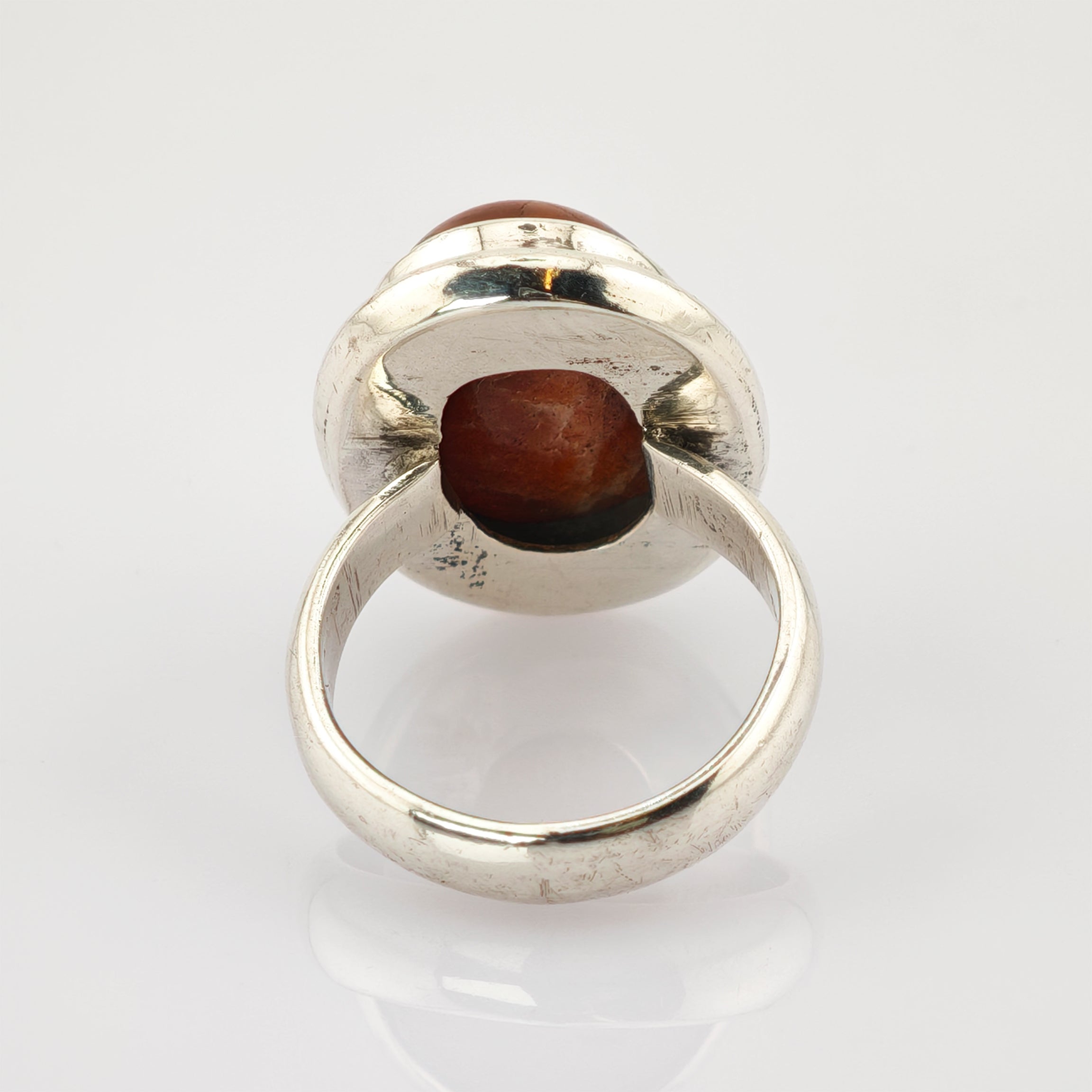 Silberfarbener Vintage-Ring mit großem ovalem rotbraunem Stein in Zargenfassung auf weißem Hintergrund.