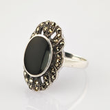 Eleganter Silberring mit ovalem schwarzen Zentralstein und Muschelmuster aus Metallstützen.
