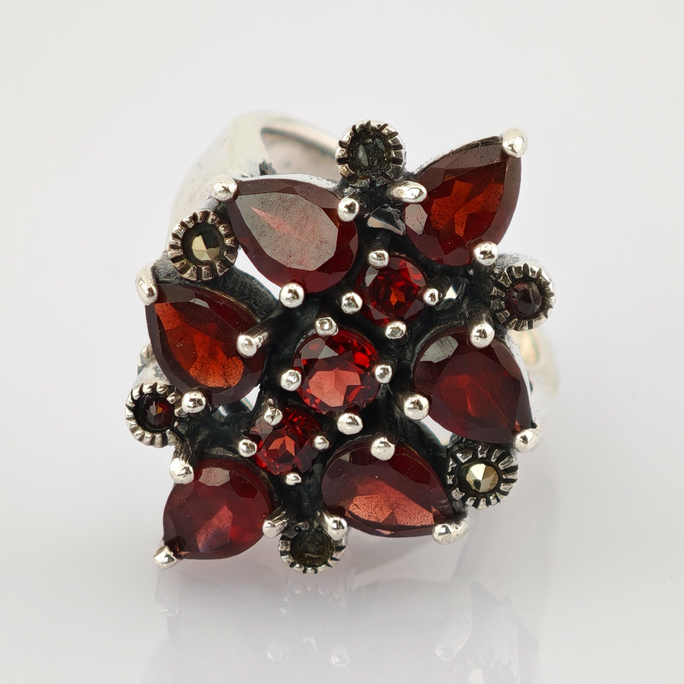 Silberring mit facettierten roten Edelsteinen im Blumenmuster.