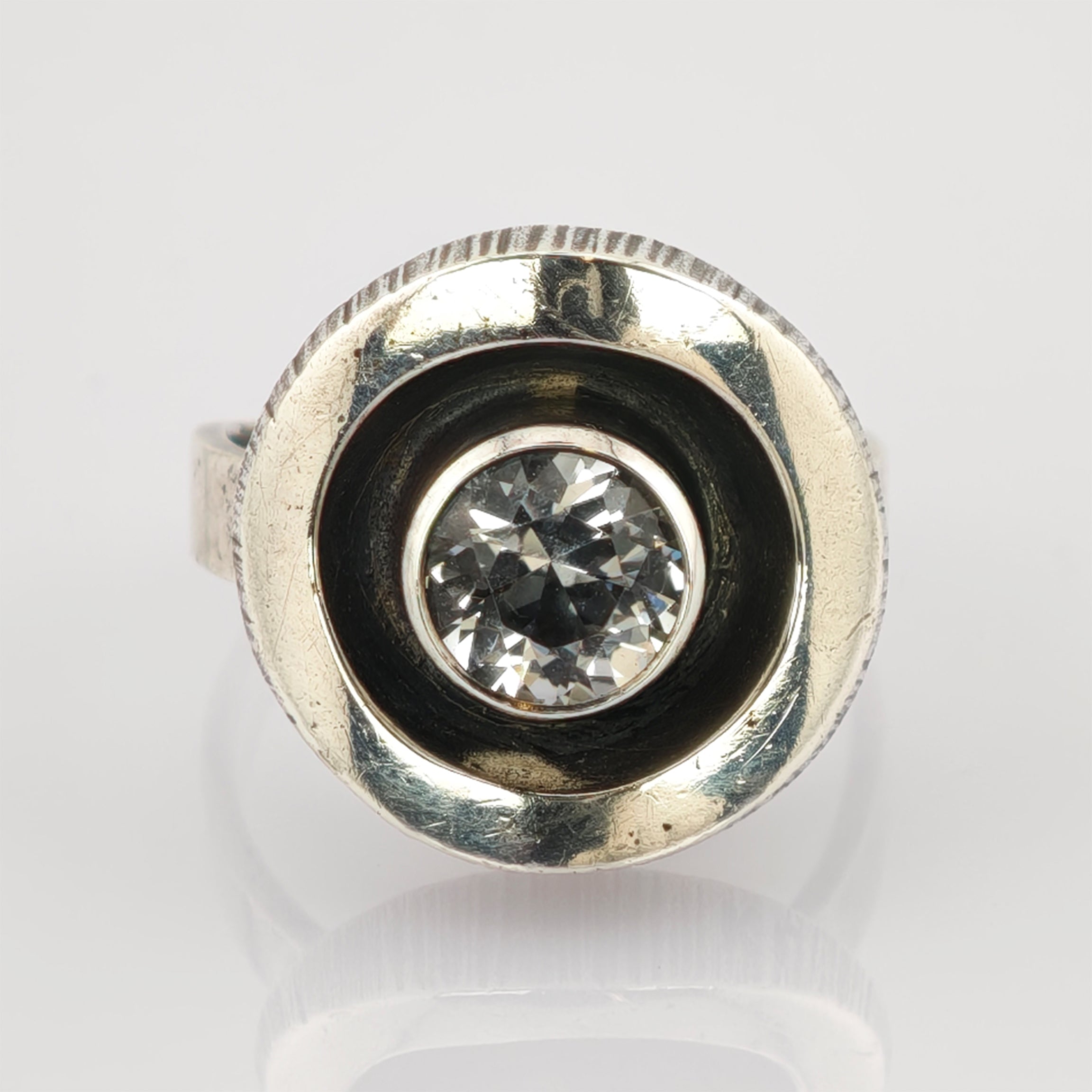 Silberring mit rundem klarem facettiertem Edelstein in konkaver Fassung und matter Oberfläche.