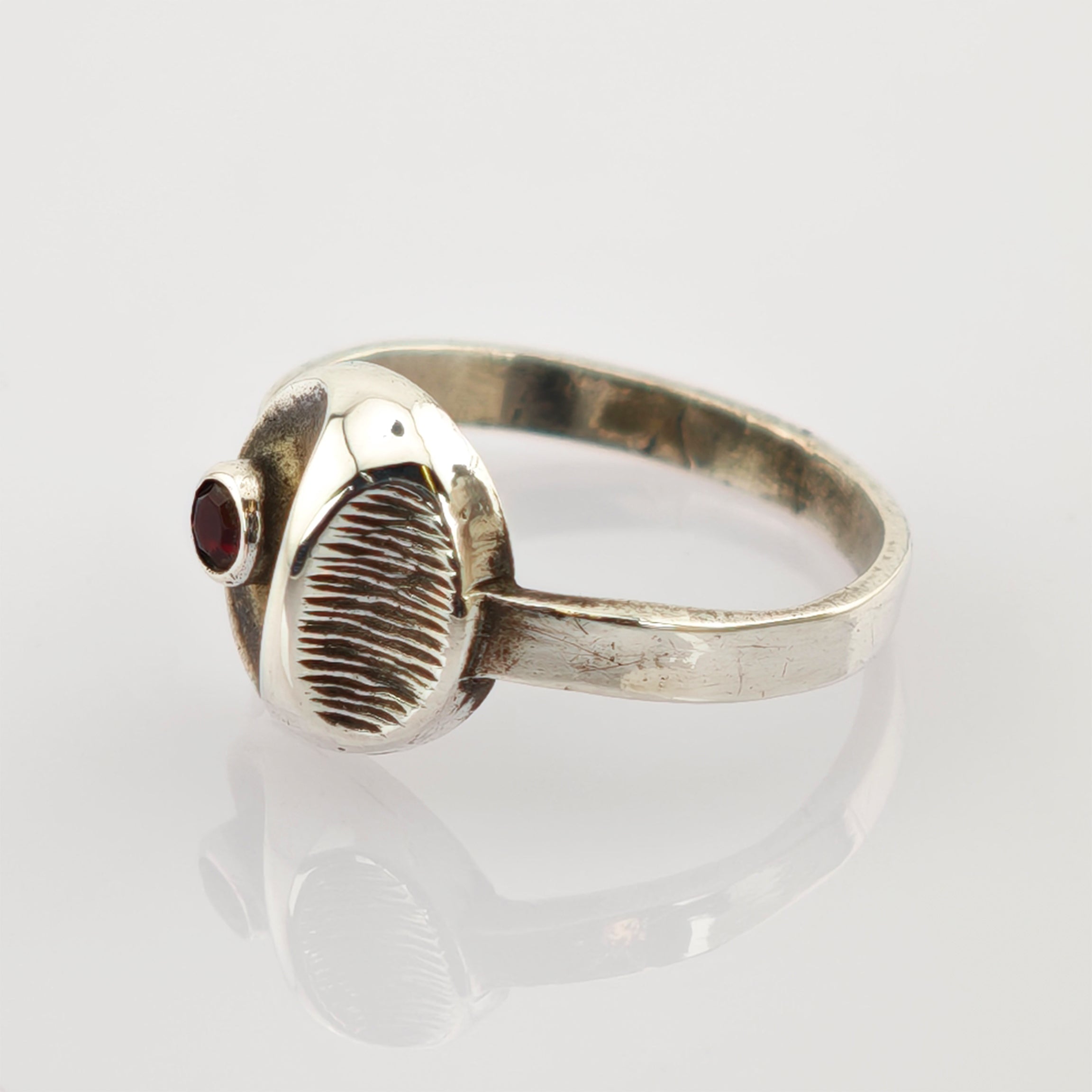 Silberring mit strukturiertem ovalem Mittelteil und kleinem rundem rotem Edelstein