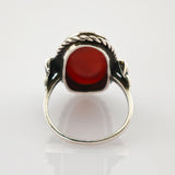 Silberring mit tiefrotem ovalem Edelstein und gedrehter Seilstruktur auf weißem Hintergrund.