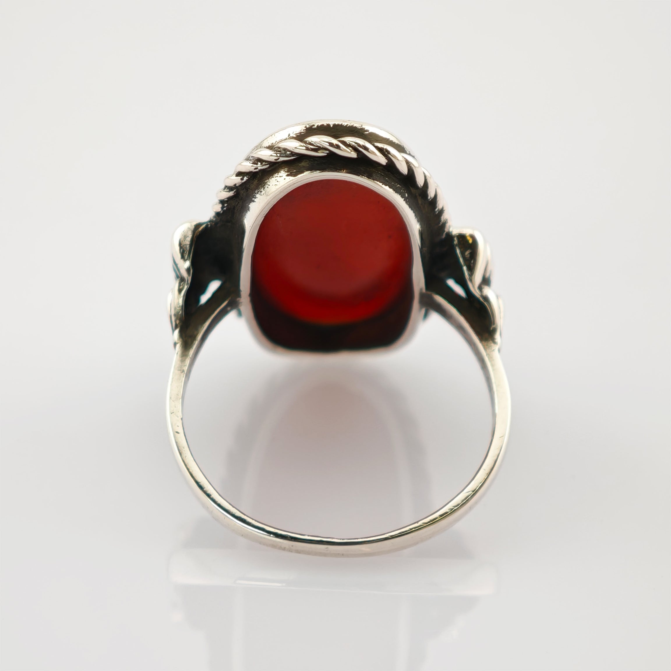 Silberring mit tiefrotem ovalem Edelstein und gedrehter Seilstruktur auf weißem Hintergrund.
